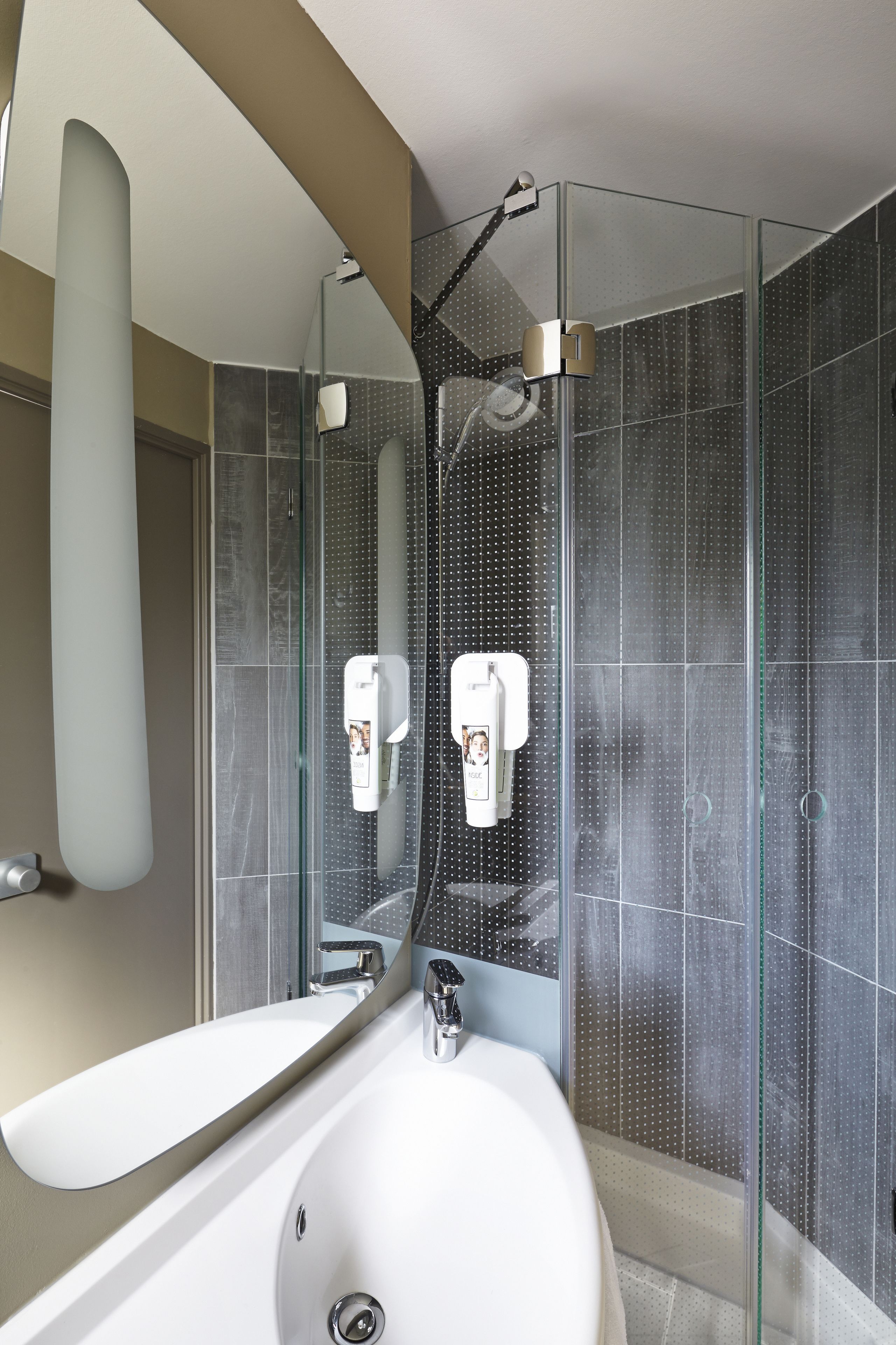Un baño moderno con un espejo grande, un lavabo blanco y una zona de ducha con paredes de vidrio.