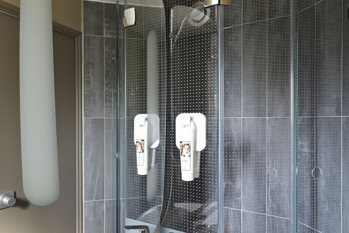 A modern bathroom with a large mirror, a white sink, and a glass-enclosed shower area.