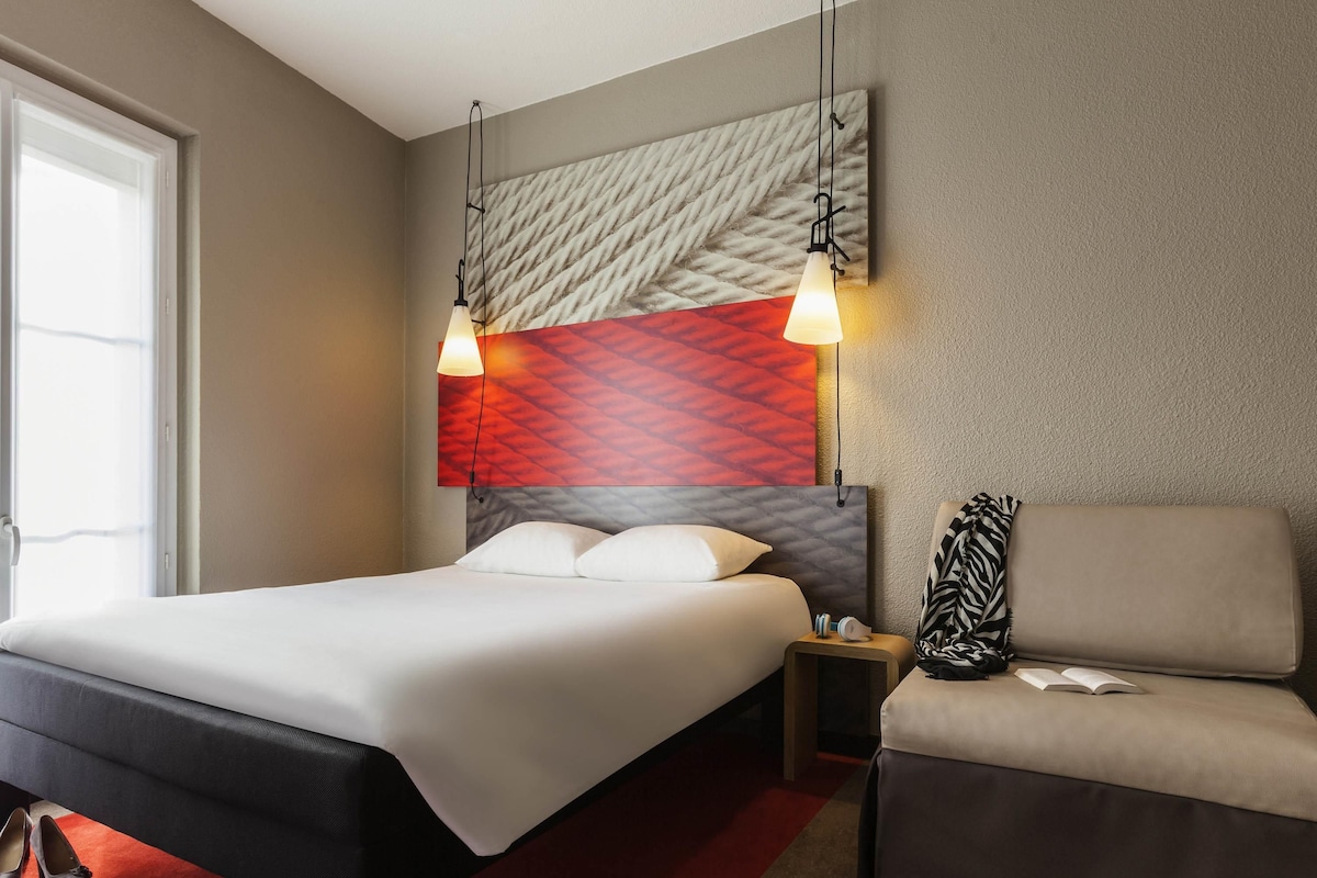A hotel room with a bed, bedside table, and a sofa.