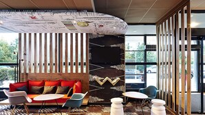 A modern interior with a wooden floor, a sofa with red cushions, a rocking chair, and a patterned rug.