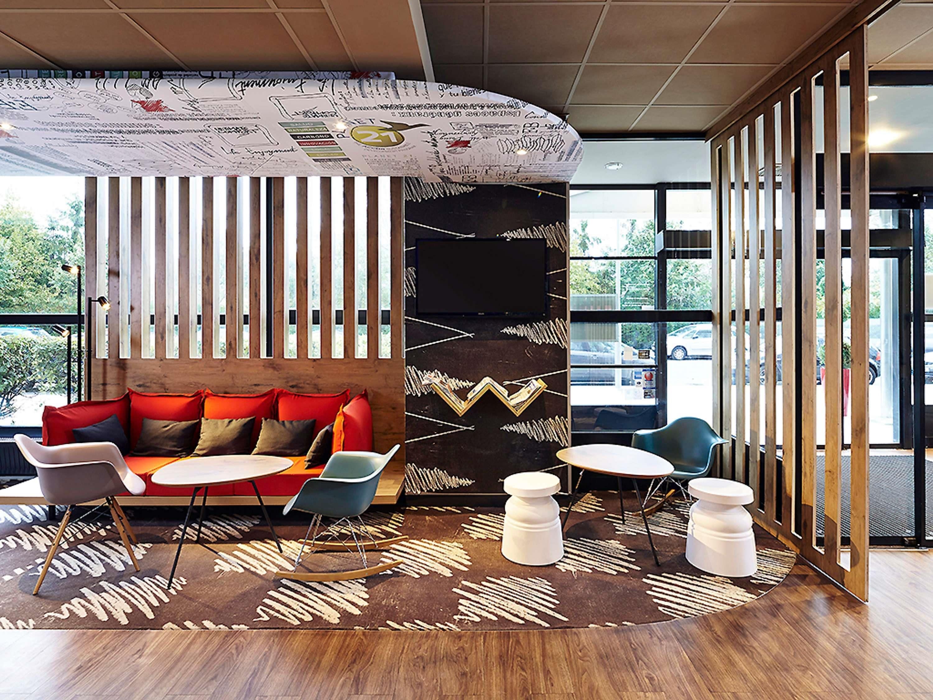 Een modern interieur met een houten vloer, een bank met rode kussens, een schommelstoel en een kamerkleed met een patroon.