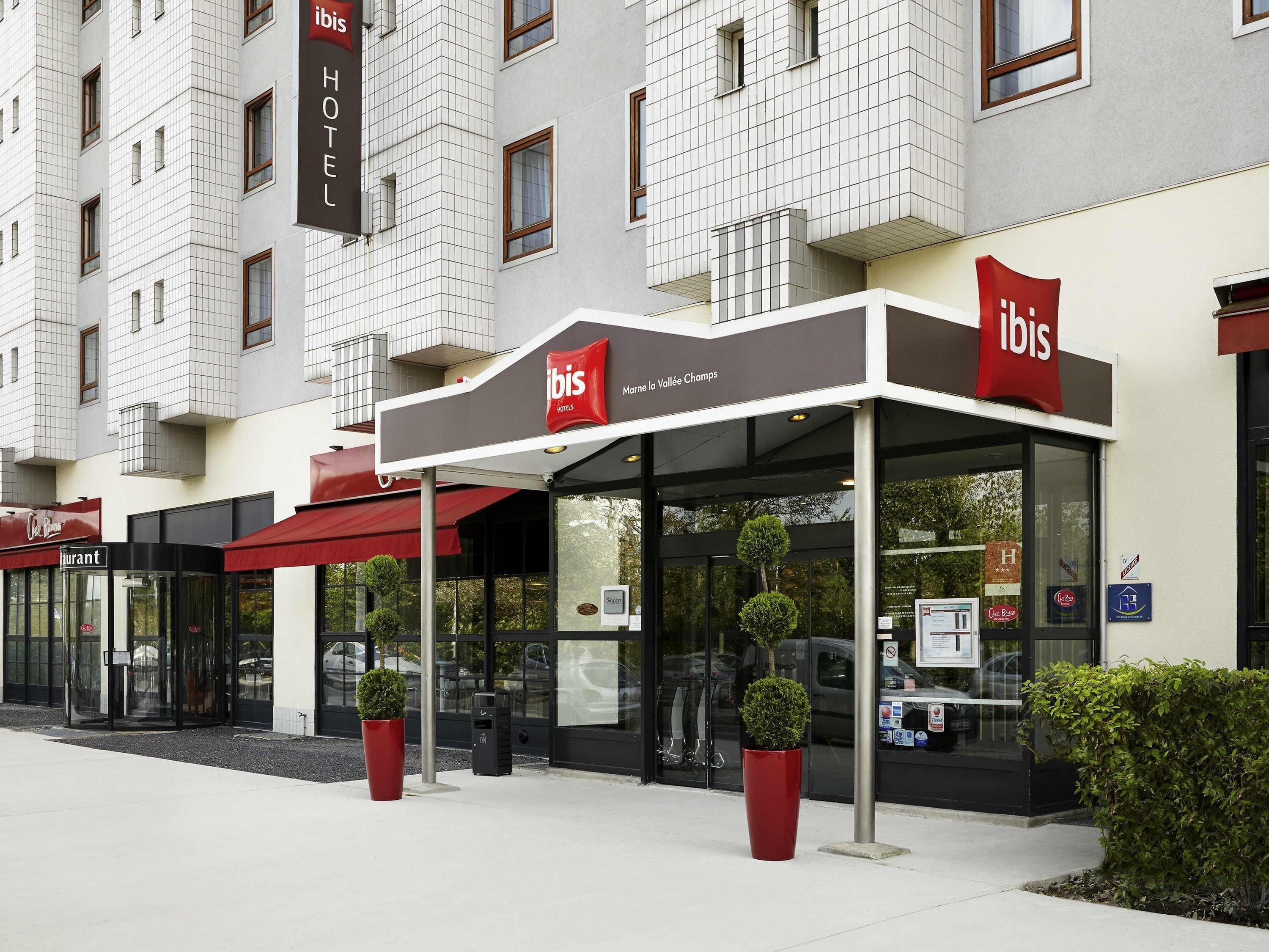 Un hotel con fachada moderna, entrada de vidrio y toldos rojos.