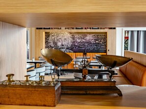 Un restaurante con diseño moderno, que presenta una gran pared de pizarra con ecuaciones científicas y un mural, mesas y sillas de madera, y un horno de ladrillo.