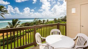 A balcony with a white table and chairs, overlooking a beach with palm trees and the ocean.