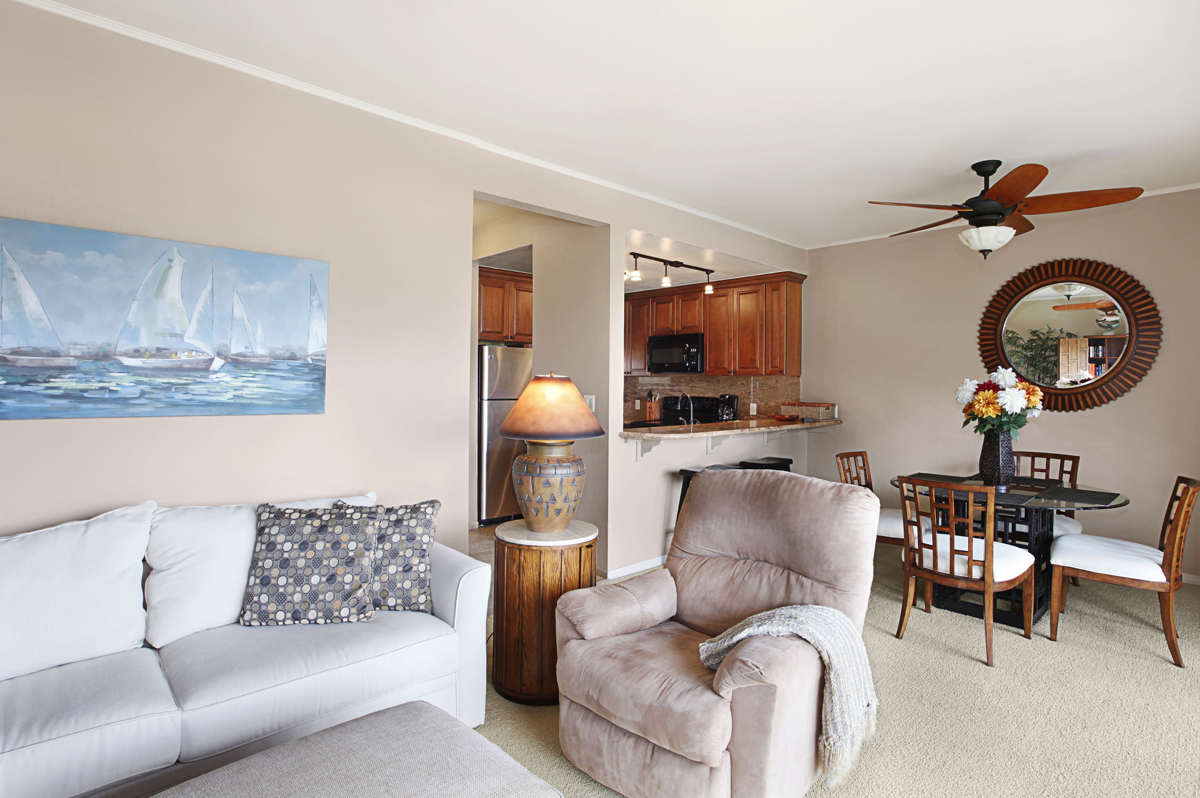 A living room with a sofa, armchair, lamp, and a painting of sailboats.