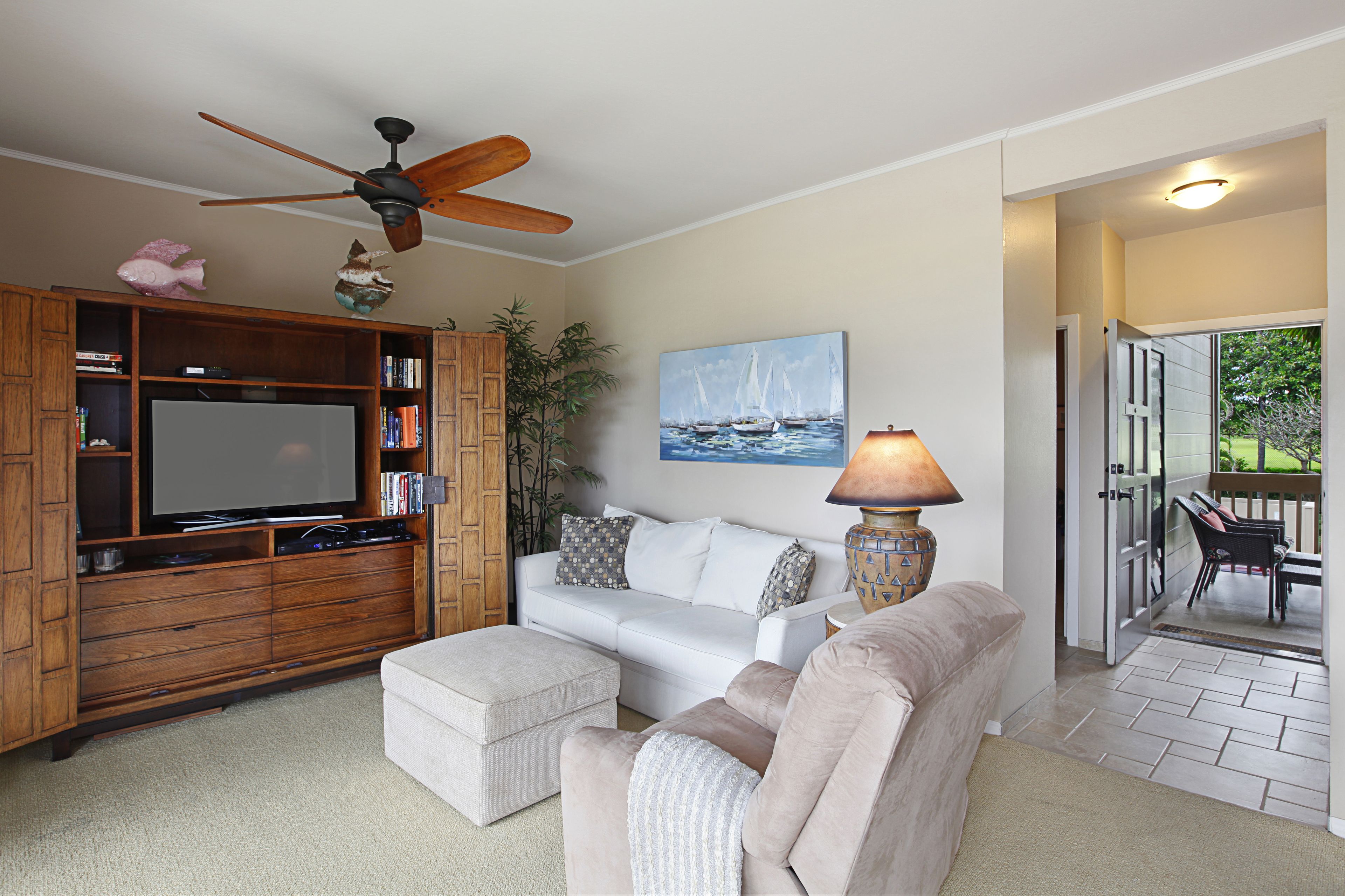 A living room with a flat-screen TV, wooden entertainment center, white sofa, and a ceiling fan.