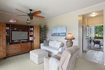 A modern living room with a wooden entertainment unit, a dining area with a wooden table and chairs, and a kitchen in the background. at Castle Kaha Lani Resort