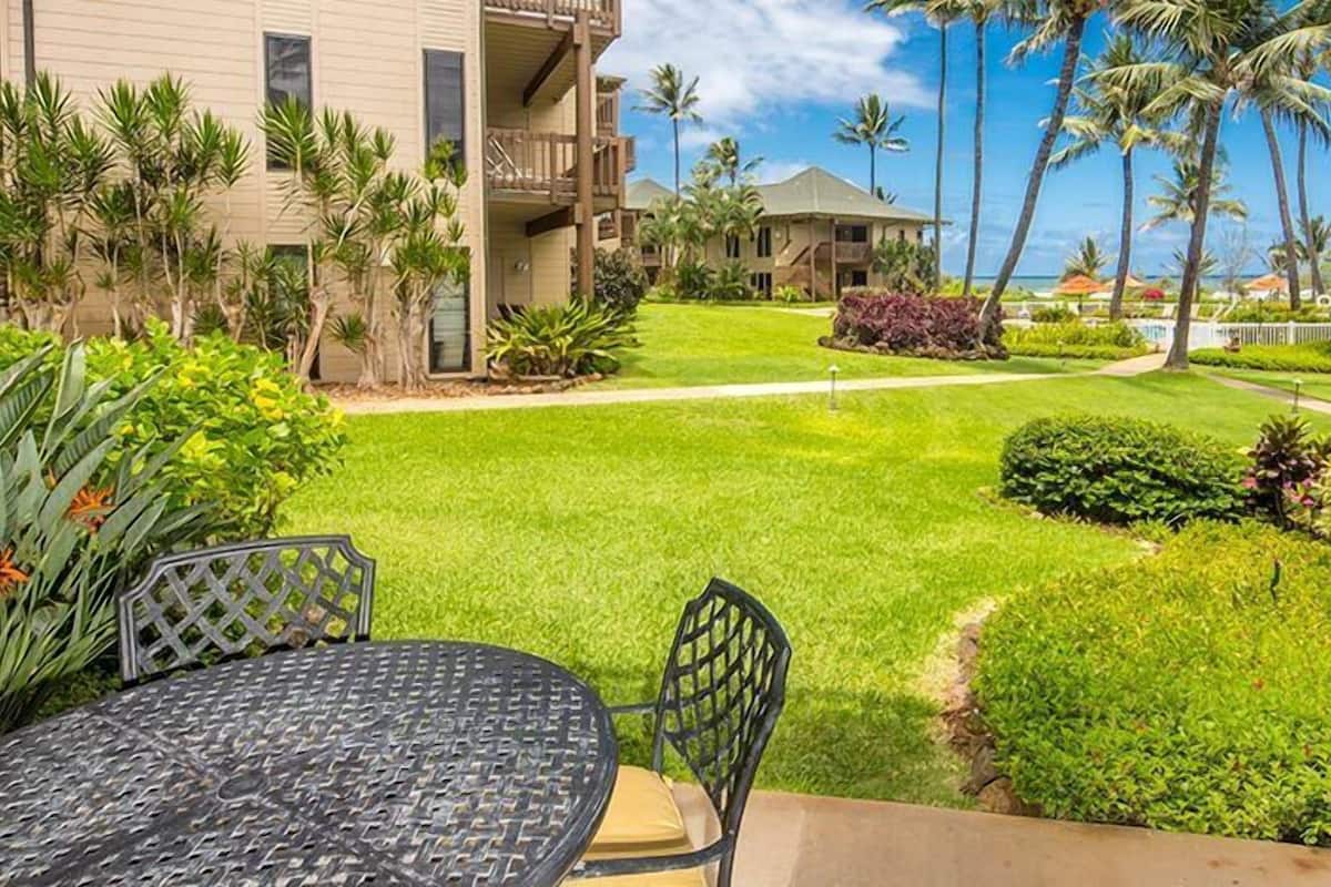 A hotel courtyard with a dining area, palm trees, and a view of the ocean.