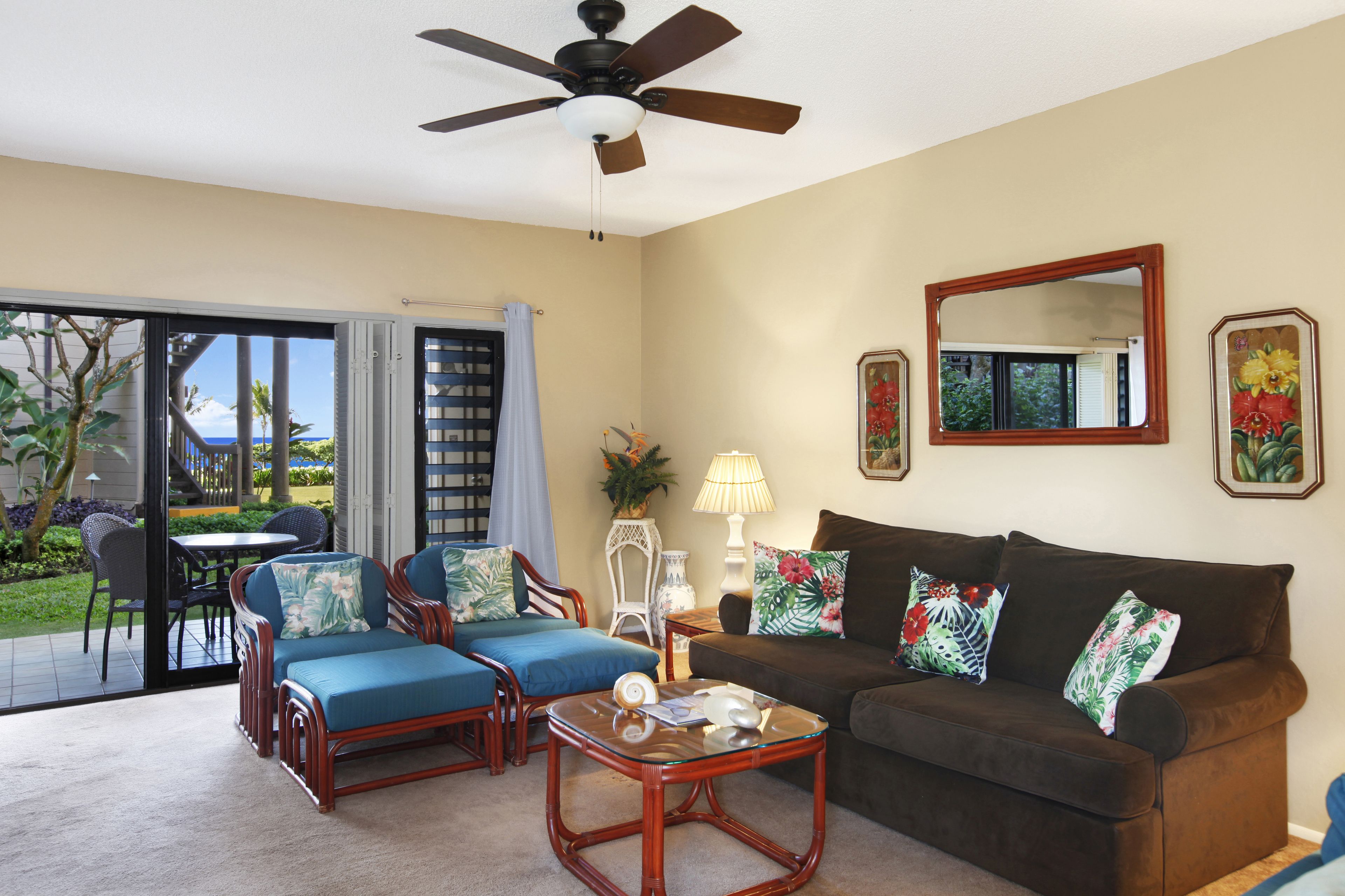 A living room with a brown sofa, blue chairs, a glass coffee table, and a ceiling fan.