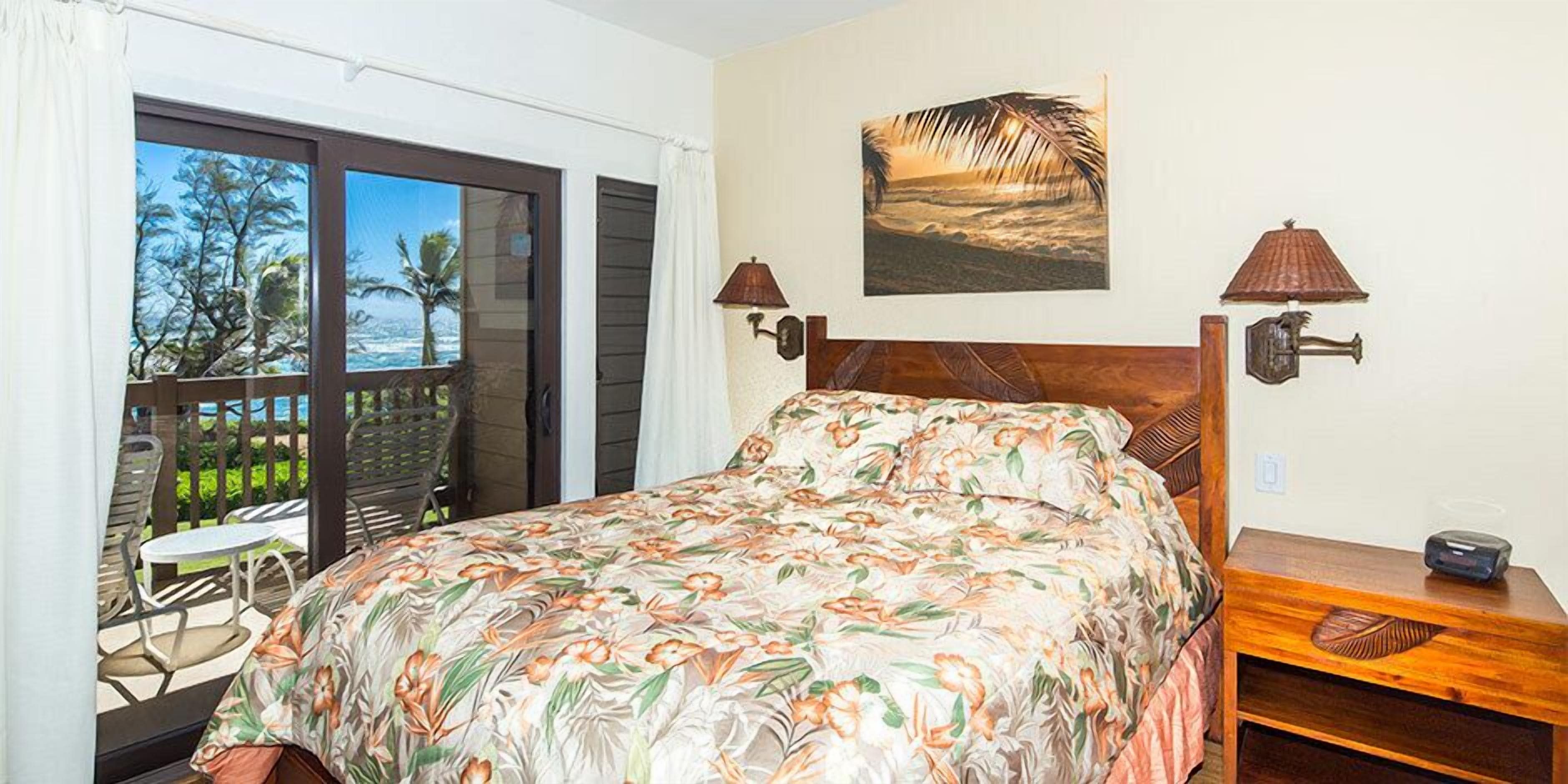 A bedroom with a bed, a balcony with chairs, and a painting of a beach scene.