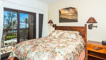 A bedroom with a bed, a balcony with chairs, and a painting of a beach scene.