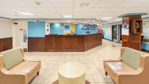 A reception area with a wooden reception desk, two beige sofas with patterned cushions, and a central round table. - Days Inn by Wyndham Raleigh-Airport-Research Triangle Park (Morrisville)