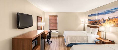 A hotel room with a flat-screen TV, a desk with a chair, two beds, a nightstand with a lamp, and a large window with blinds.