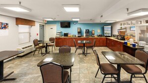 A cafeteria with tables and chairs, a counter with a coffee machine, and a television on the wall. - Days Inn by Wyndham Raleigh-Airport-Research Triangle Park (Morrisville)