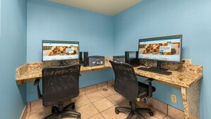 A room with two desks, each with a computer and speakers, and a blue wall. - Days Inn by Wyndham Raleigh-Airport-Research Triangle Park (Morrisville)