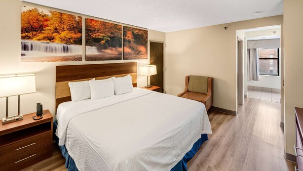 A hotel room with a large bed, two bedside tables with lamps, a wooden headboard, and three autumn-themed wall art pieces. - Days Inn by Wyndham Raleigh-Airport-Research Triangle Park (Morrisville)