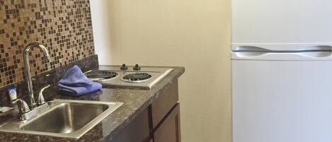 A kitchen with a double sink, two burners, a microwave, and a white refrigerator.