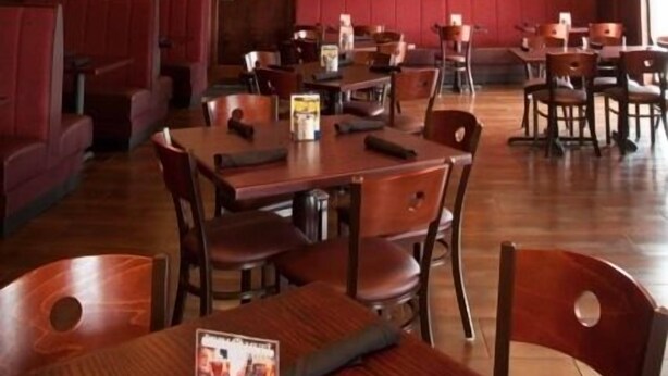 A restaurant with wooden tables and booths, a stone accent wall, and a recessed ceiling with a central light fixture.