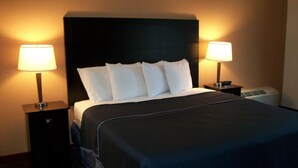 A hotel room with a large bed, two bedside lamps, a nightstand, and a wall-mounted air conditioning unit.