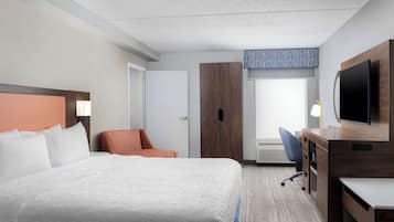 Una habitación de hotel con una cama grande, un escritorio con televisor, una silla y un armario.