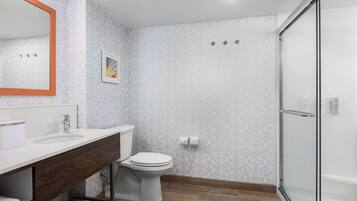 A modern bathroom with a white toilet, a sink with a wooden vanity, a glass shower enclosure, and patterned walls.