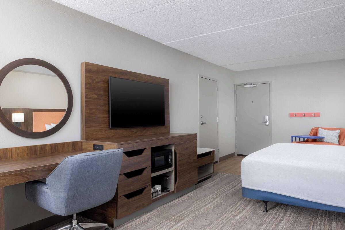 A hotel room with a bed, a desk with a chair, a television, a microwave, and a wardrobe.