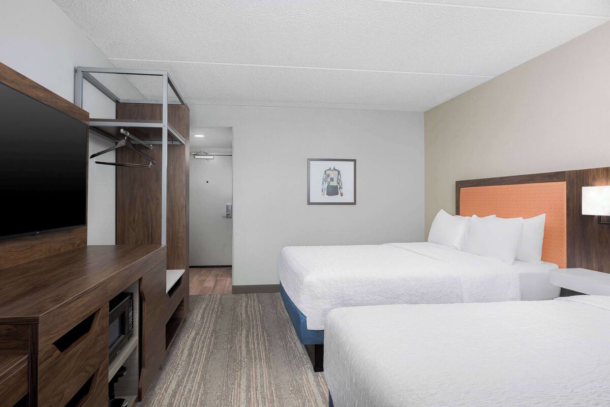 A hotel room with two beds, a TV, a wardrobe, and a framed picture on the wall.