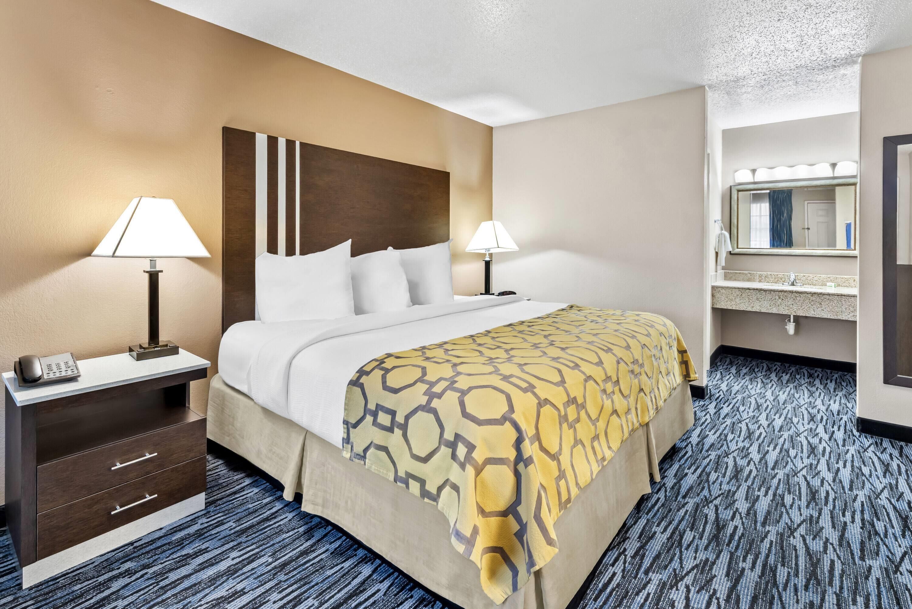 A hotel room with a bed, two bedside tables with lamps, a telephone, a mirror, and a bathroom with a sink and mirror.