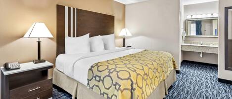 A hotel room with a bed, two bedside tables with lamps, a telephone, a mirror, and a bathroom with a sink and mirror.