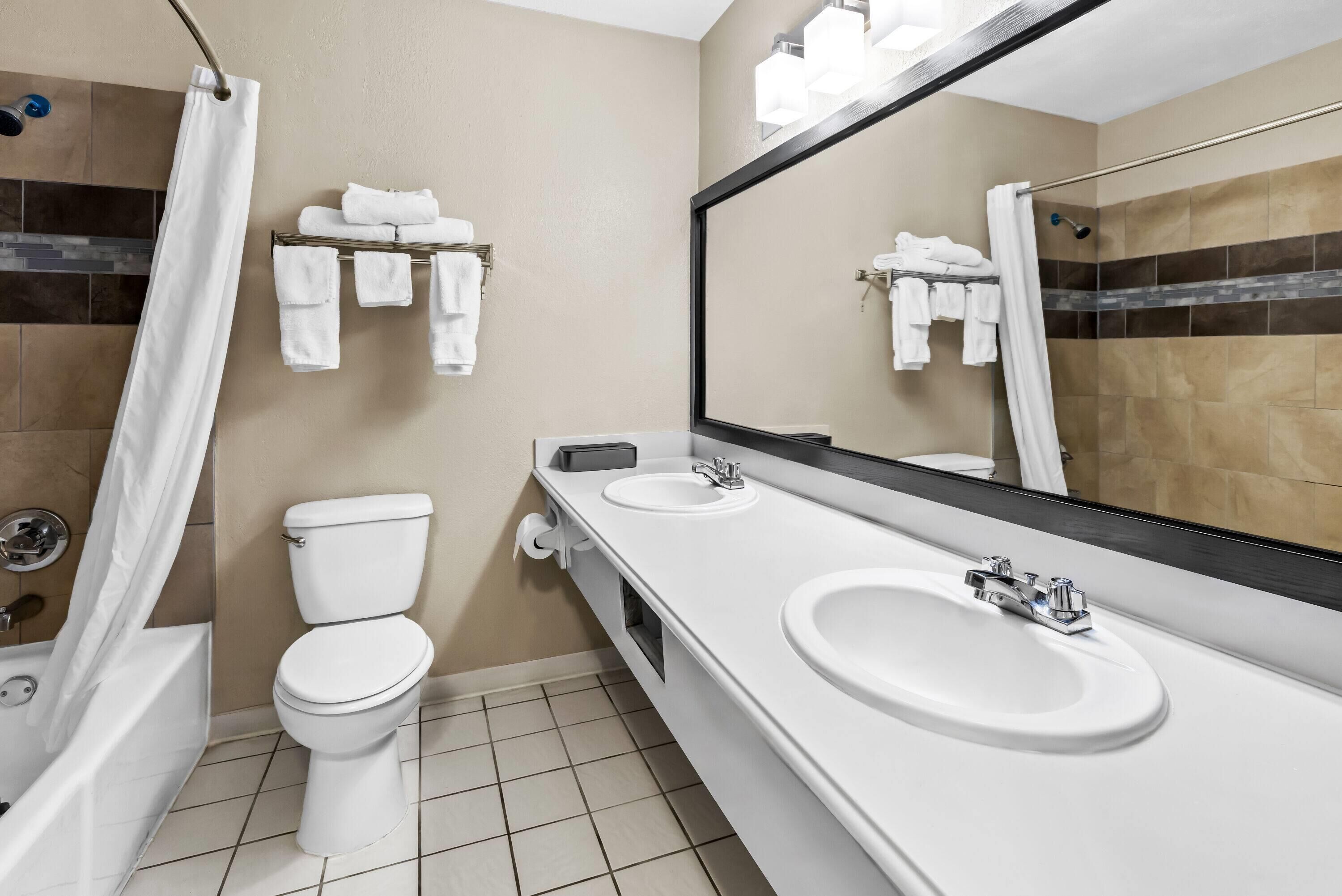 A modern bathroom with a bathtub, toilet, and two sinks.