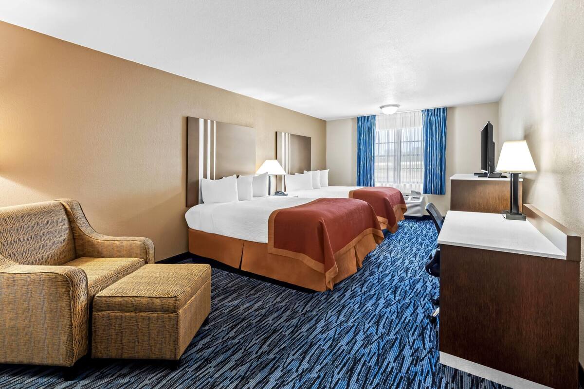 A hotel room with a large bed, a sofa, a desk, and a view of the city through the window.