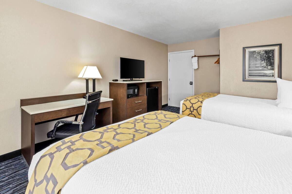 A hotel room with two beds, a desk with a chair, a television, a microwave, and a door with a coat rack.