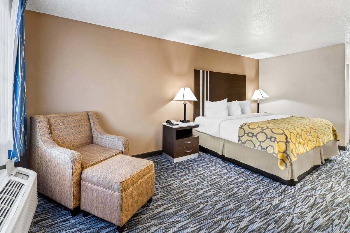 A hotel room with a bed, two bedside tables, a chair, and a heater.