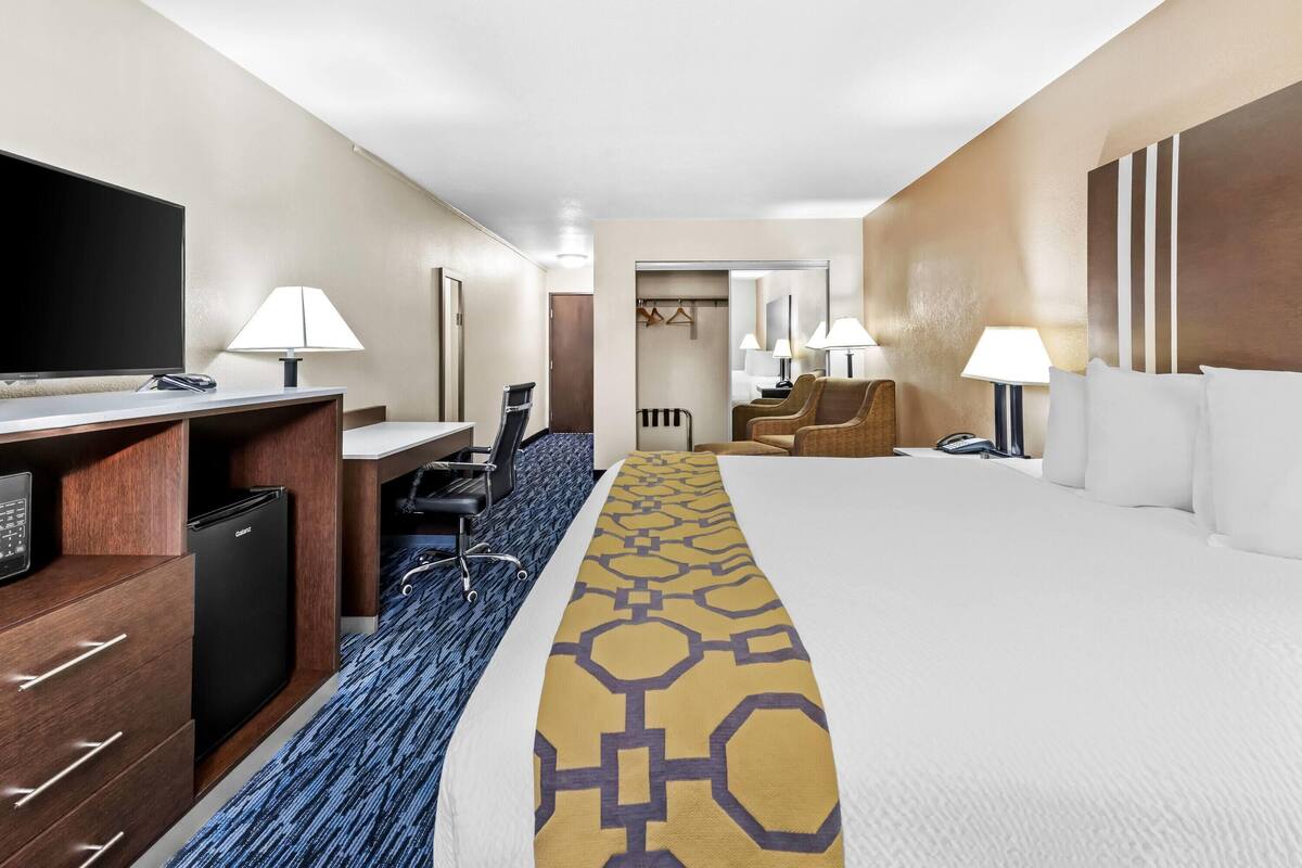 A hotel room with a bed, a desk with a computer, a TV, and a minibar.
