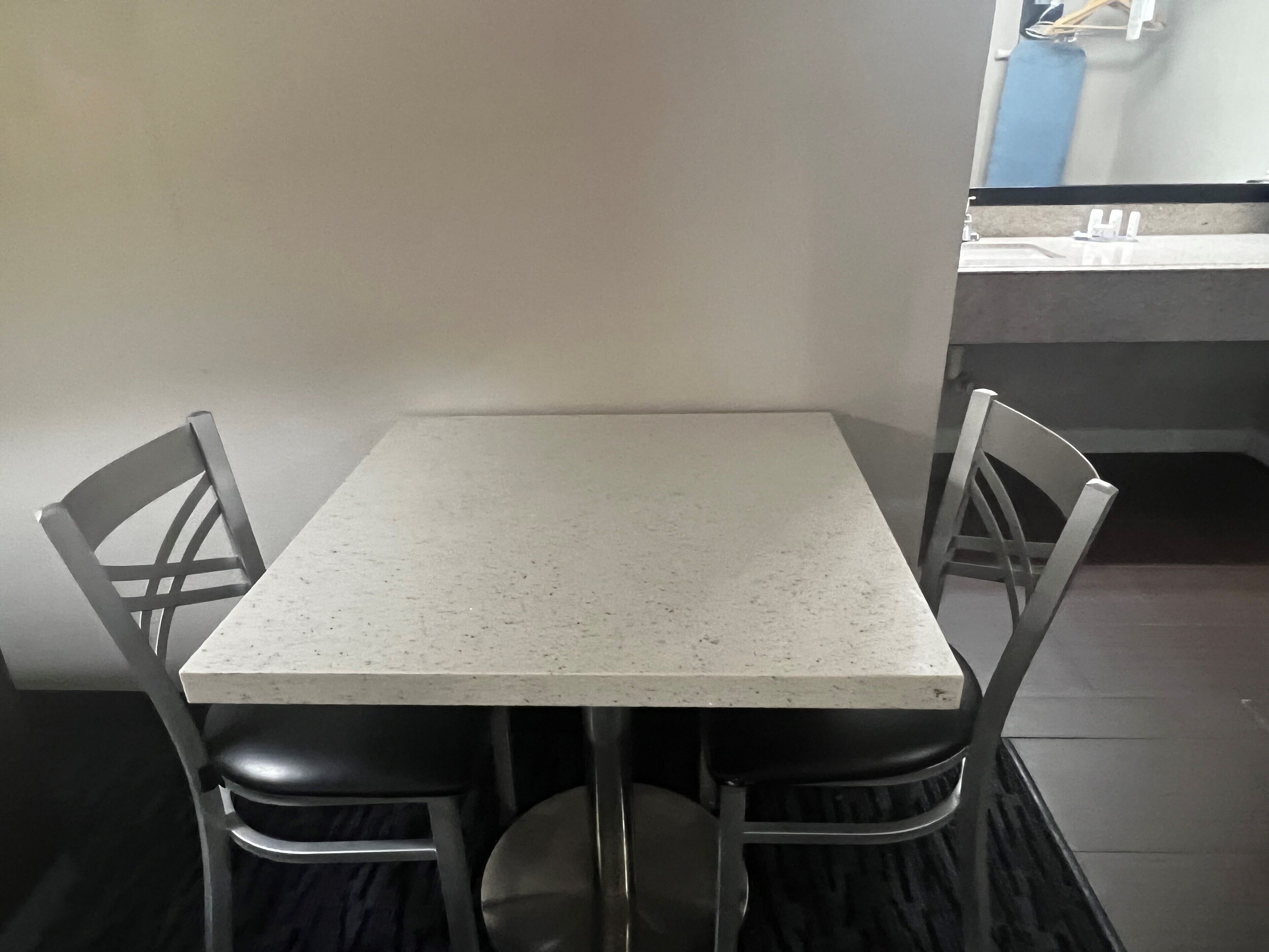 A small, square table with four chairs, a white countertop, and a sink in the background.