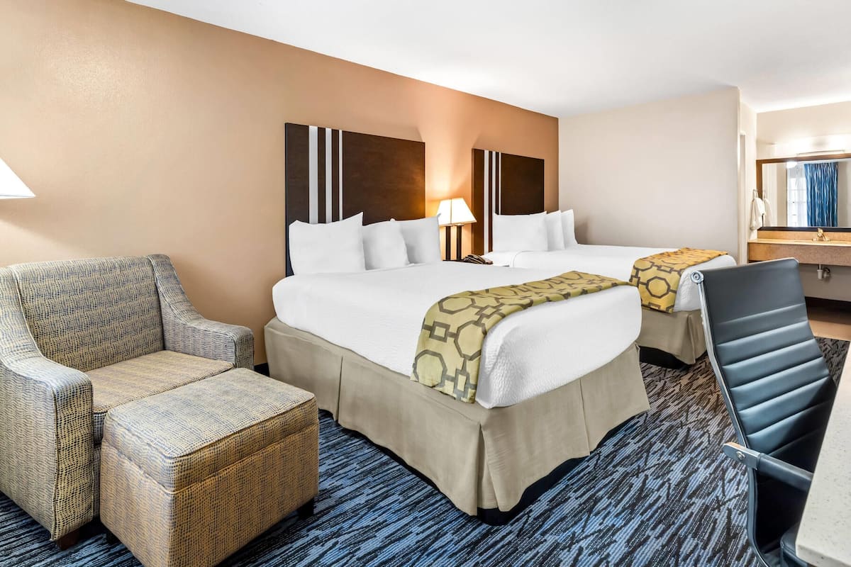 A hotel room with two beds, a sofa, a chair, a desk, and a mirror.