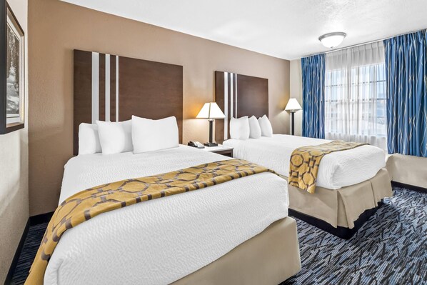 A hotel room with two beds, a large window with blue curtains, and a patterned carpet.