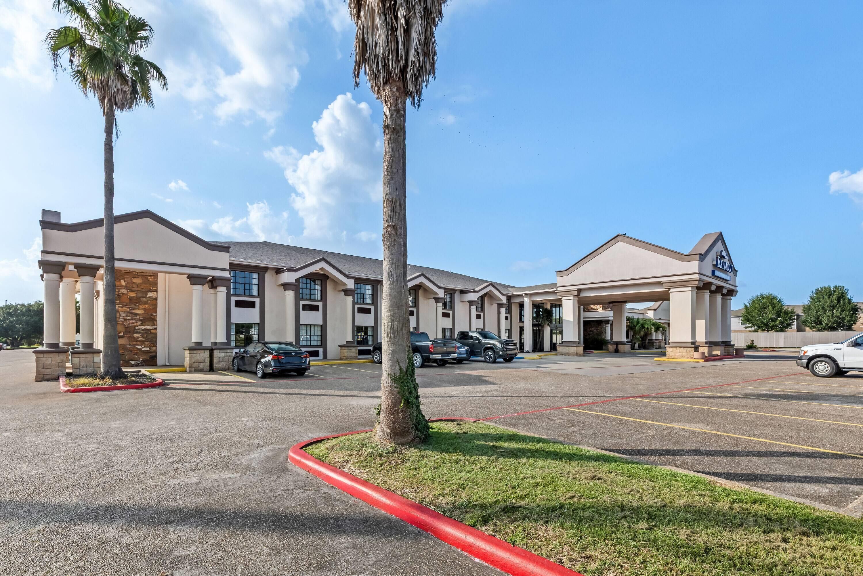 A hotel with a parking lot, multiple buildings, and palm trees.