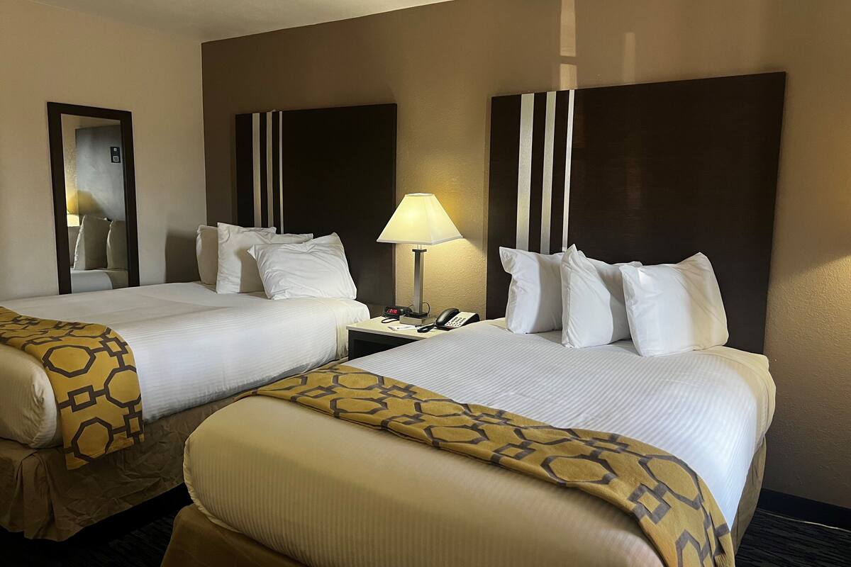 A hotel room with two beds, a nightstand with a lamp, a phone, and a mirror.
