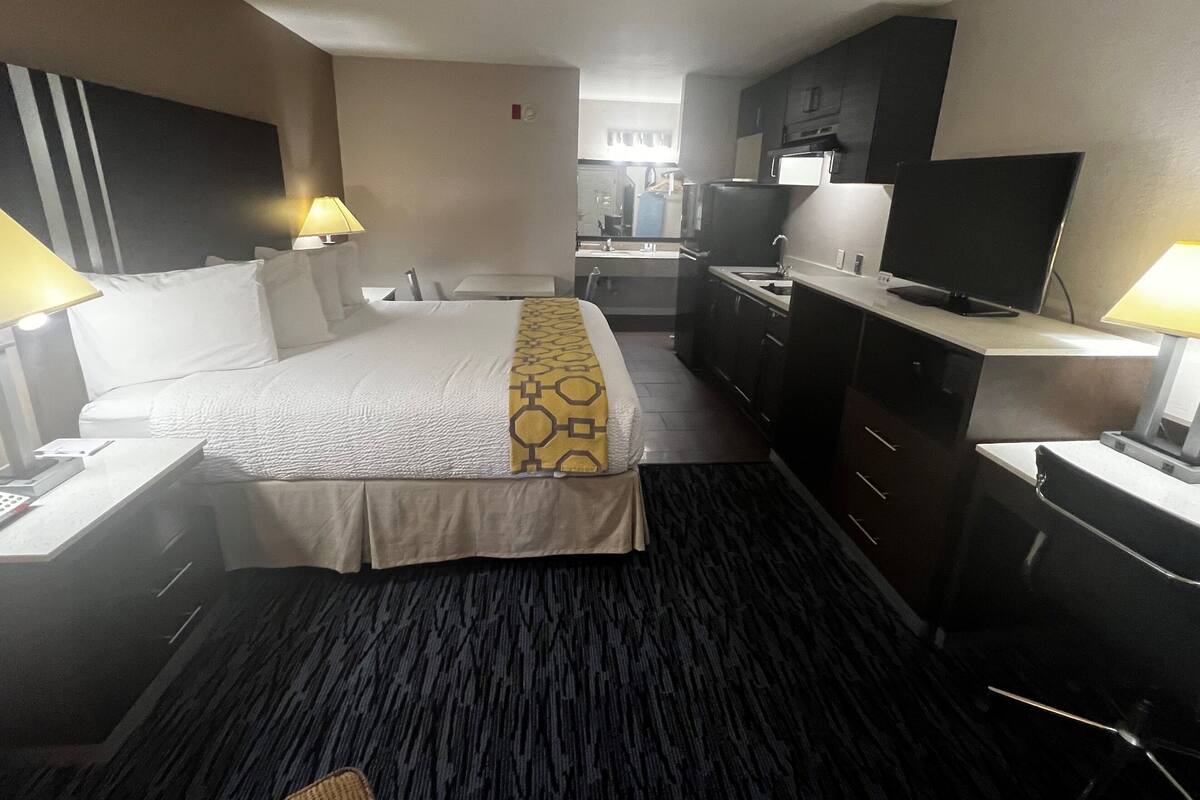 A hotel room with a bed, bedside tables, a desk, a television, and a kitchenette.