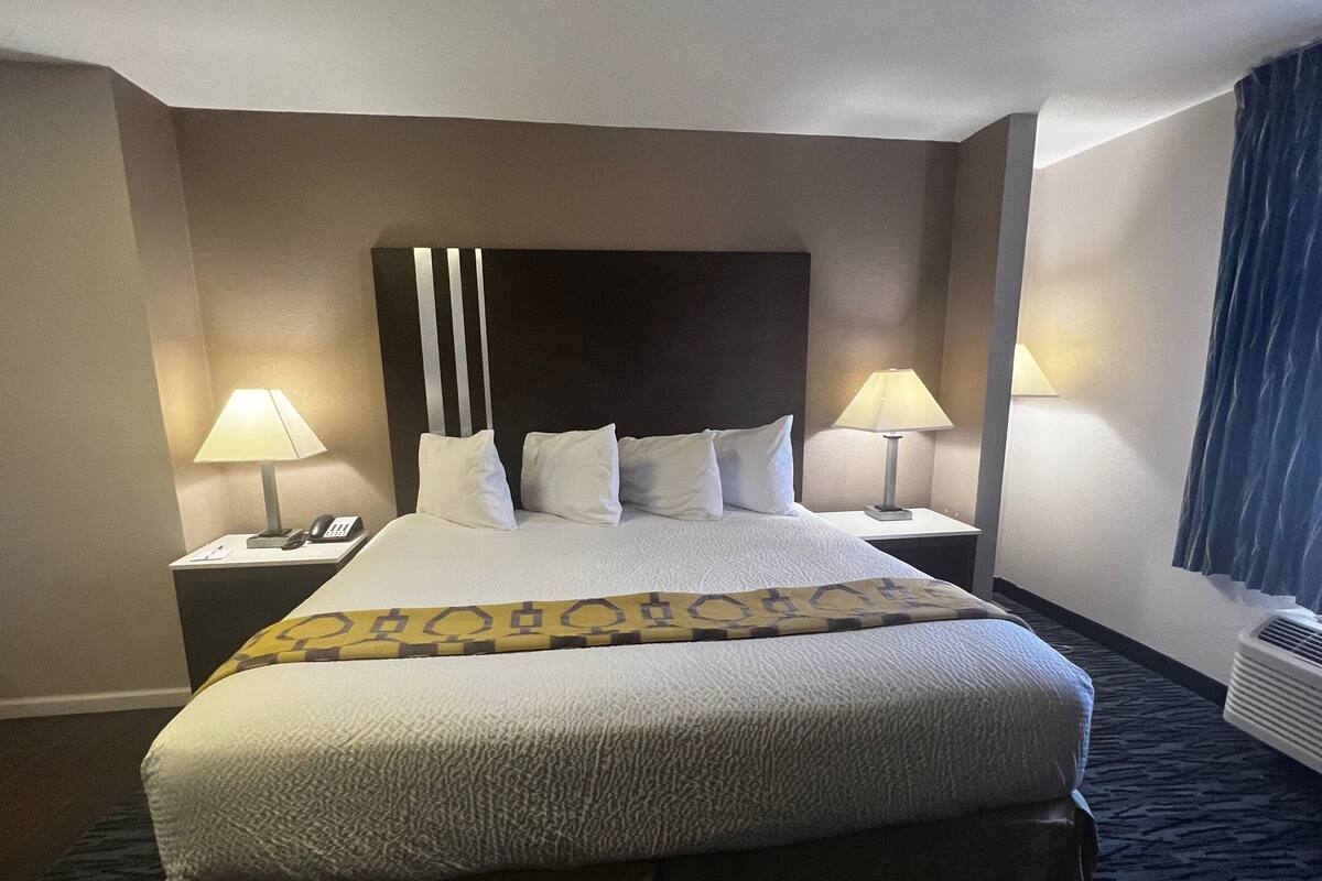 A hotel room with a large bed, two bedside tables, a telephone, and two lamps.