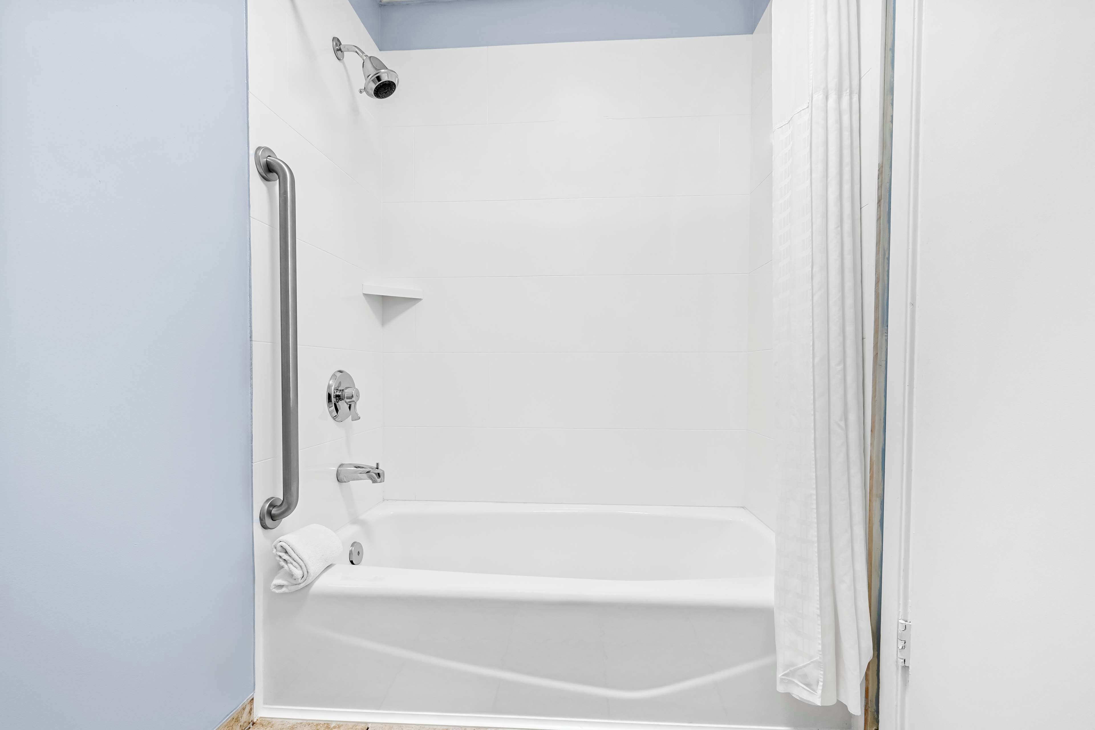 A white bathtub with a showerhead, grab bars, and a towel rack.