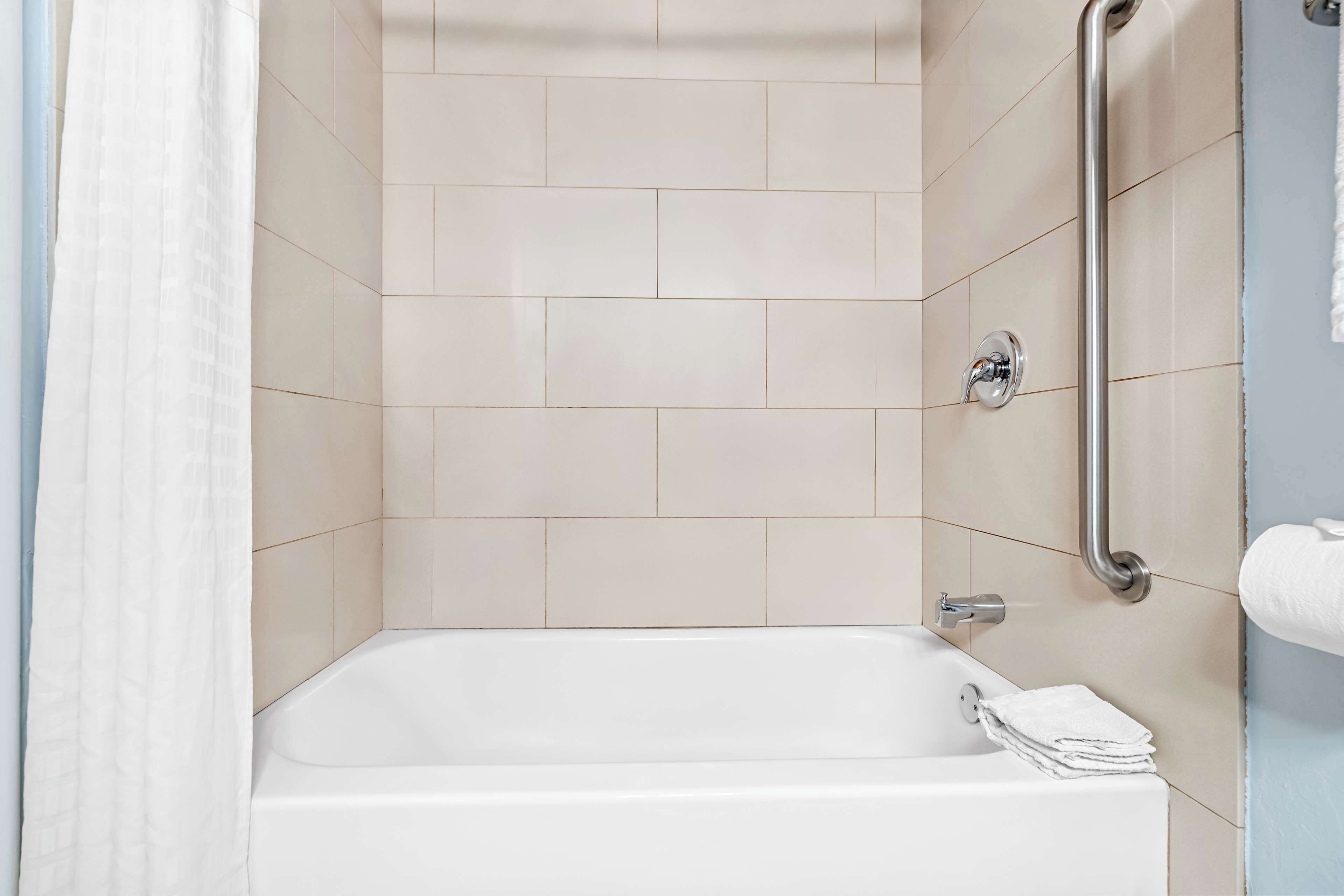 A bathroom with a bathtub, a handrail, and a towel rack.