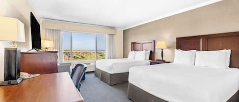 A hotel room with two beds, a desk, a chair, and a large window offering a view.