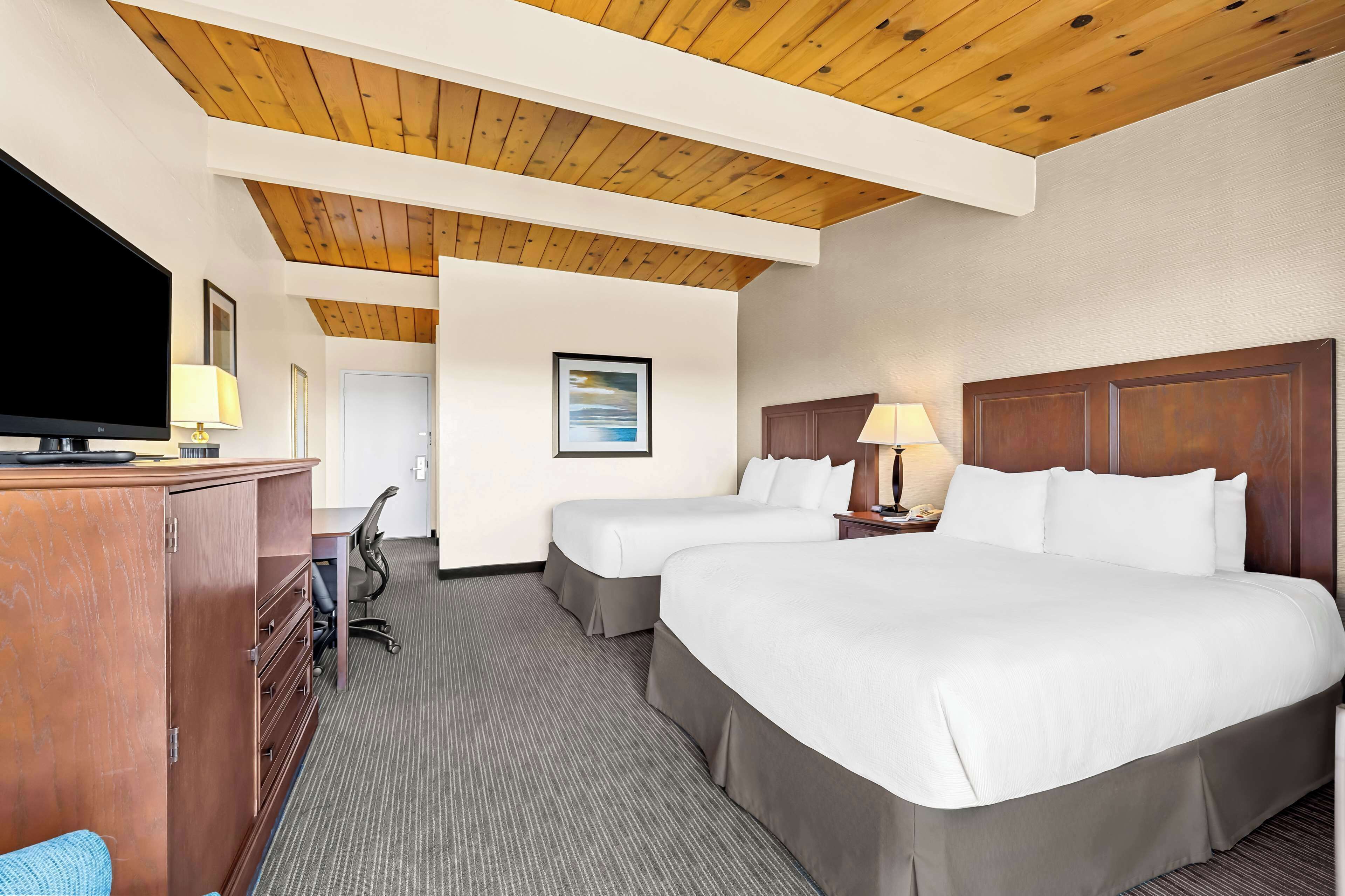 A hotel room with two beds, a desk with a TV, and a wooden ceiling.