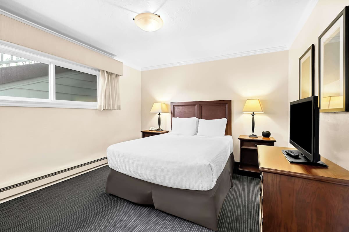 A hotel room with a large bed, two bedside lamps, a flat-screen TV, and a wooden desk.