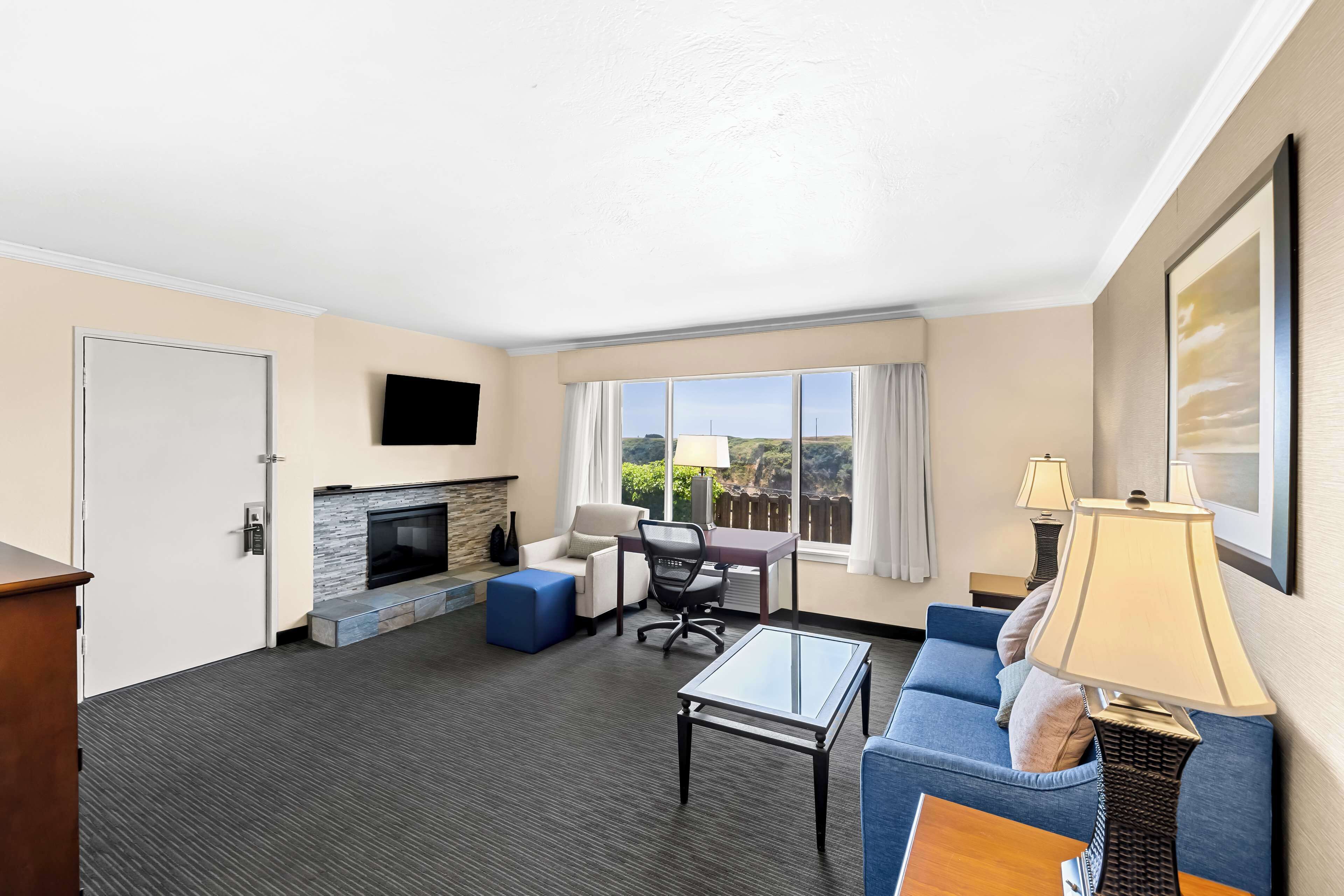 Une chambre d’hôtel équipée d’une cheminée, d’un canapé, d’une table basse, d’un bureau et d’une télévision.