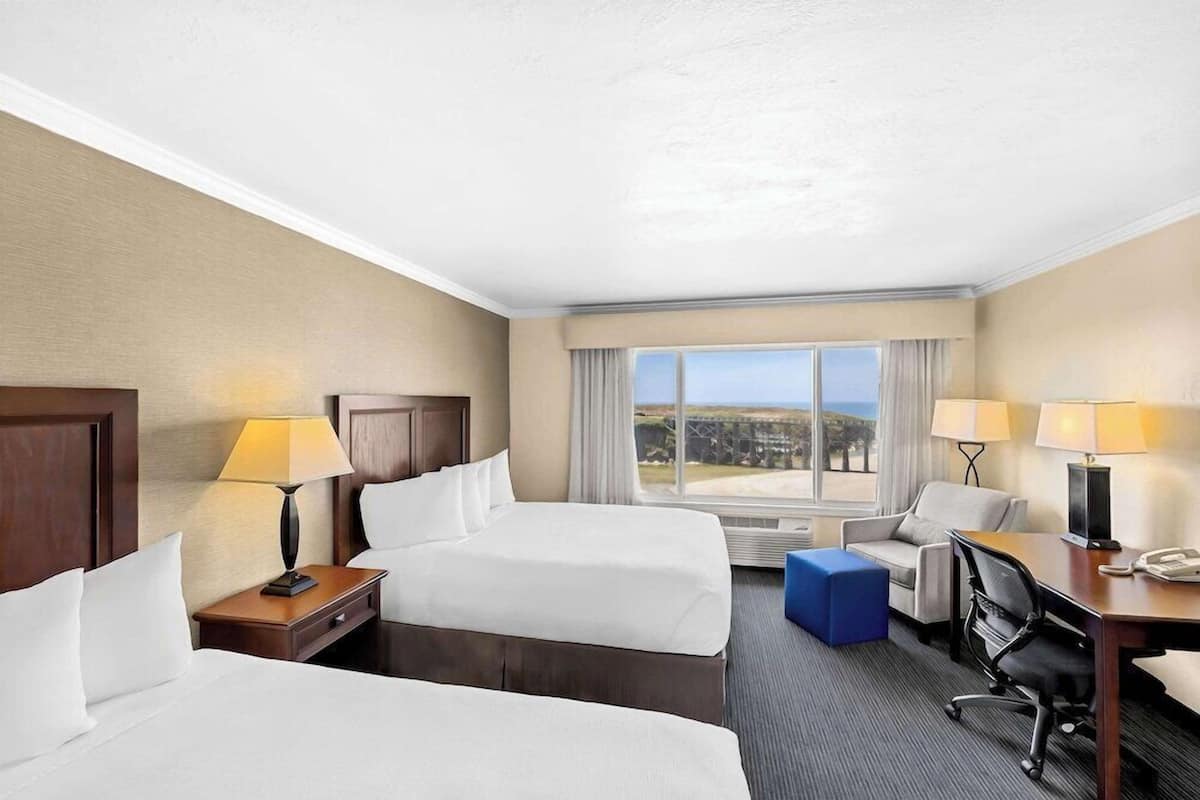 A hotel room with two beds, a desk, a chair, and a view of the landscape.