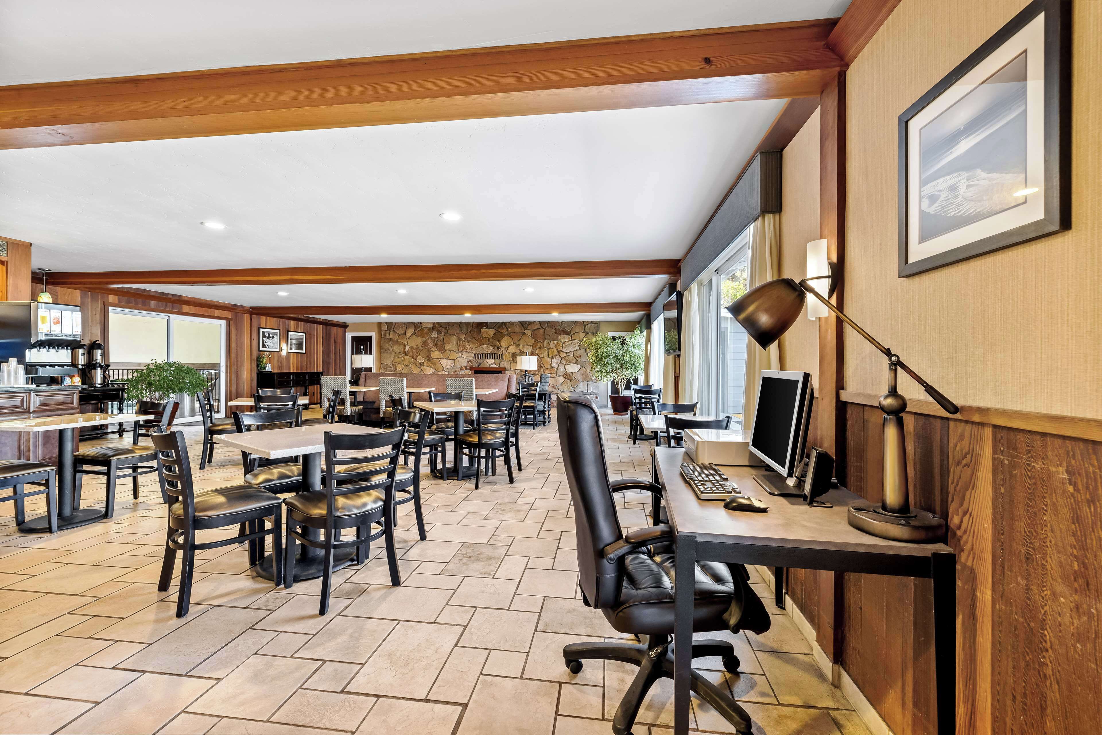 Un grand espace dédié à la salle à manger, avec plusieurs tables et chaises, un comptoir avec une caisse enregistreuse, et un mur en pierre en arrière-plan.