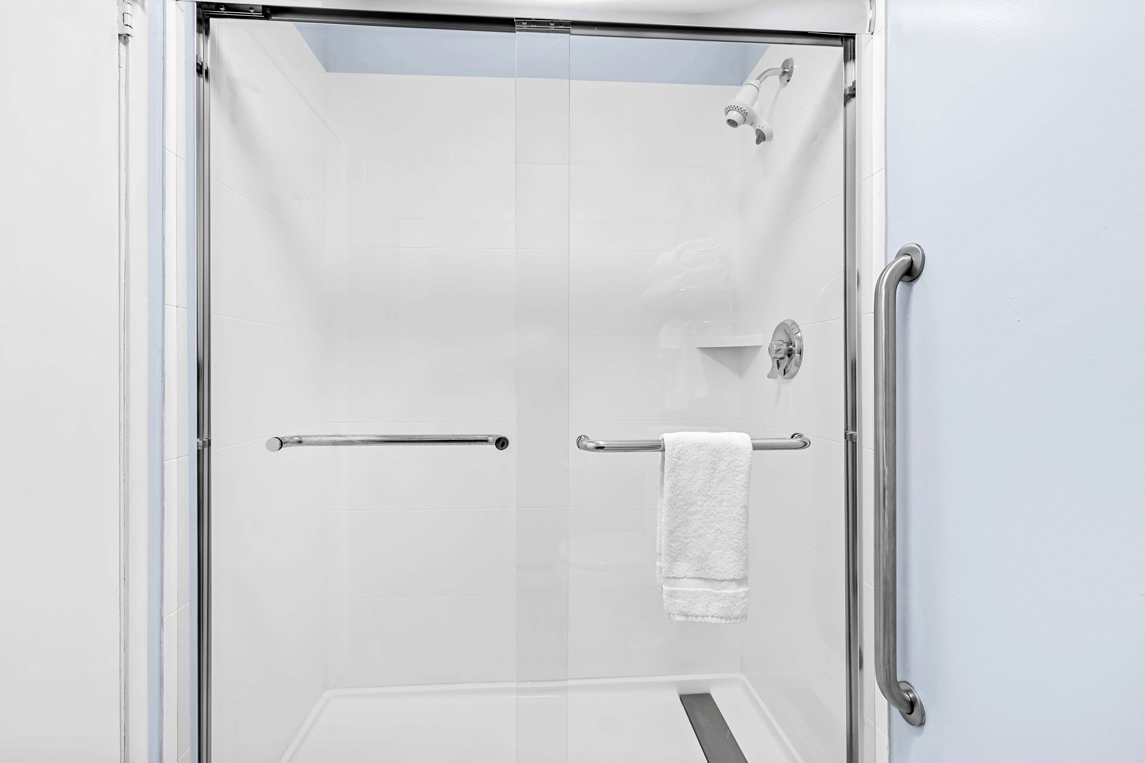 A glass-enclosed shower with a white towel hanging on a metal bar.